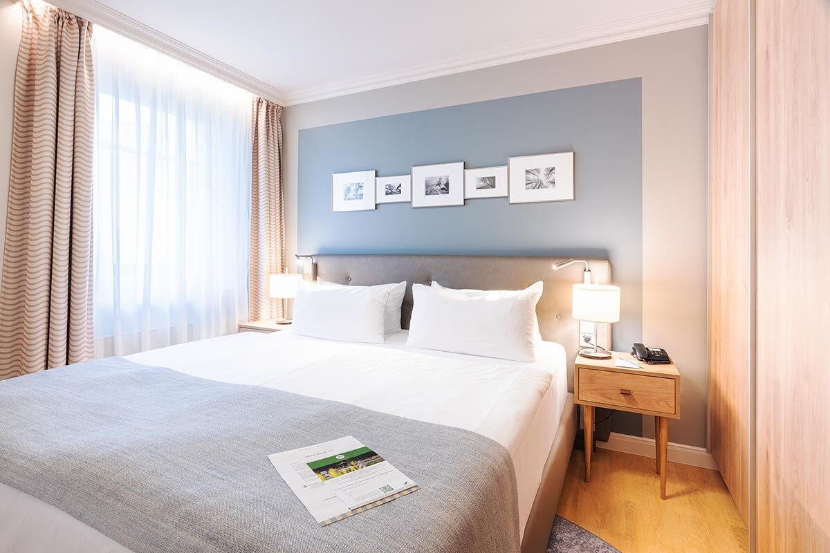 A hotel room with a large bed, a nightstand with a lamp, a phone, and a framed picture collection on the wall.