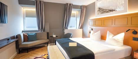 A hotel room with a large bed, a sofa, a small table, and a bench.