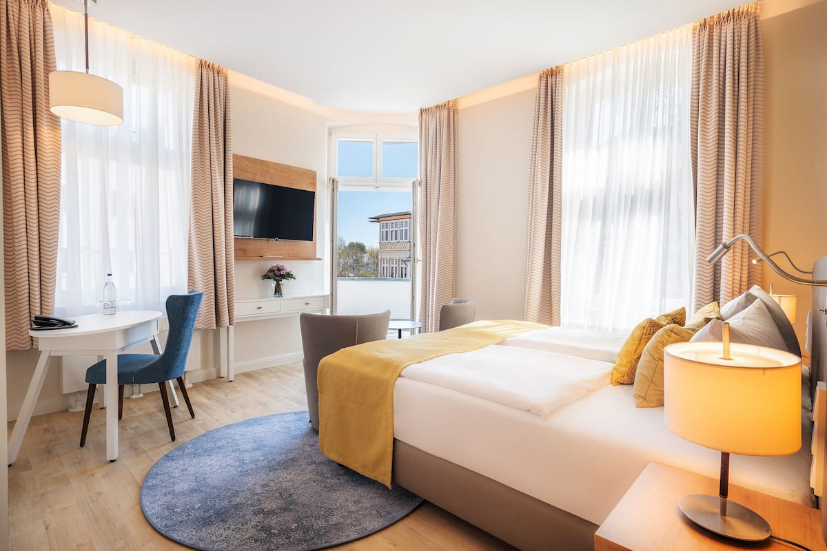 A hotel room with a bed, a desk, a chair, a TV, and a window with curtains.