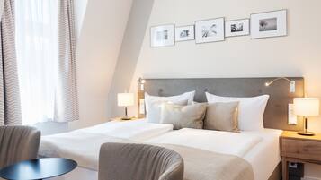 A hotel room with a large bed, two bedside tables, a chair, and a small table. There are four framed pictures on the wall.