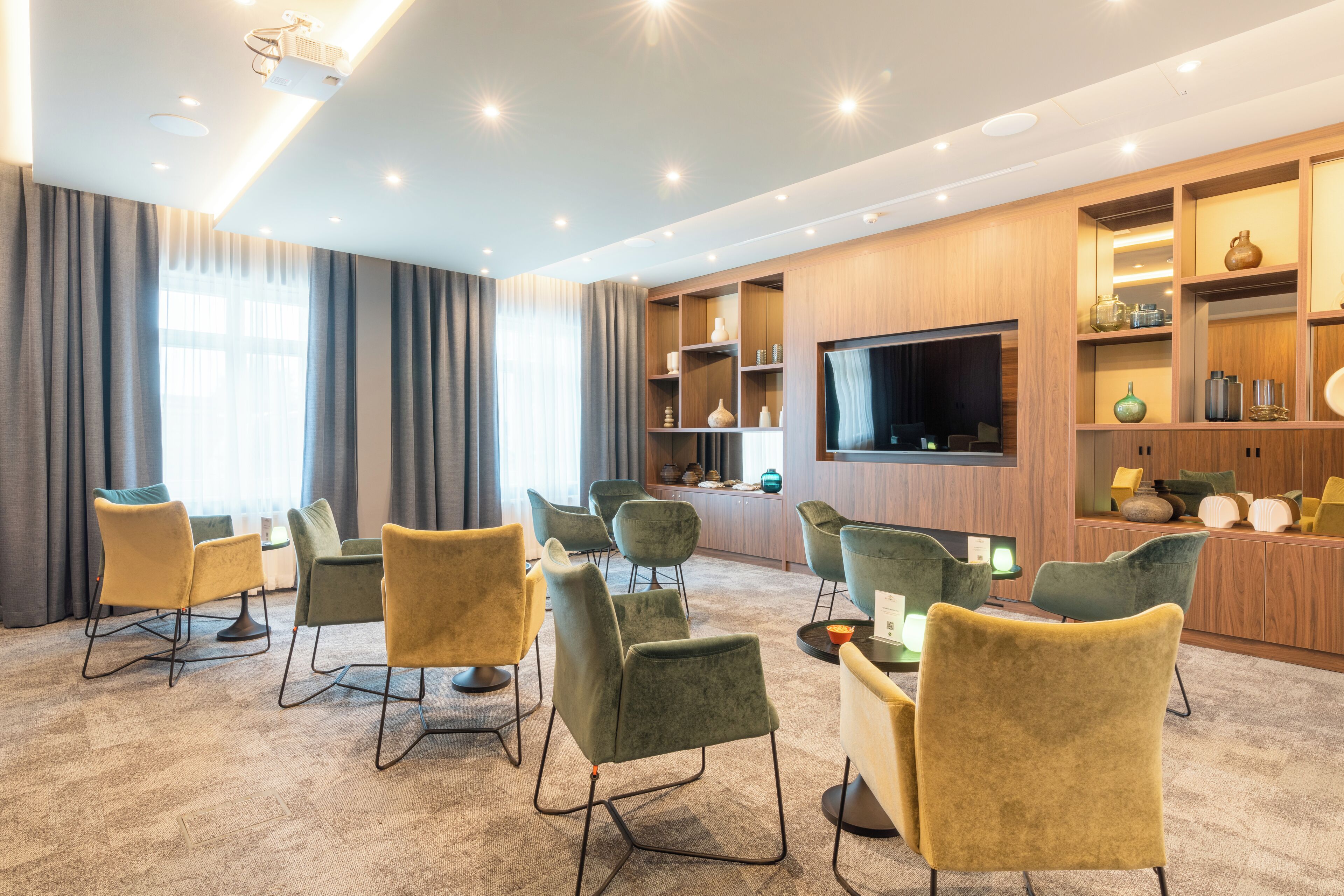 Ein modernes Hotelzimmer mit großem Flachbildfernseher, bequemen Sitzgelegenheiten und eingebauten Regalen mit Dekoration.