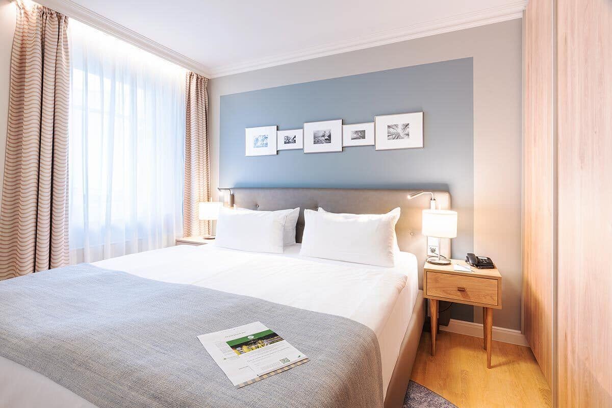 A hotel room with a large bed, a nightstand with a lamp, a phone, and a framed picture collection on the wall.