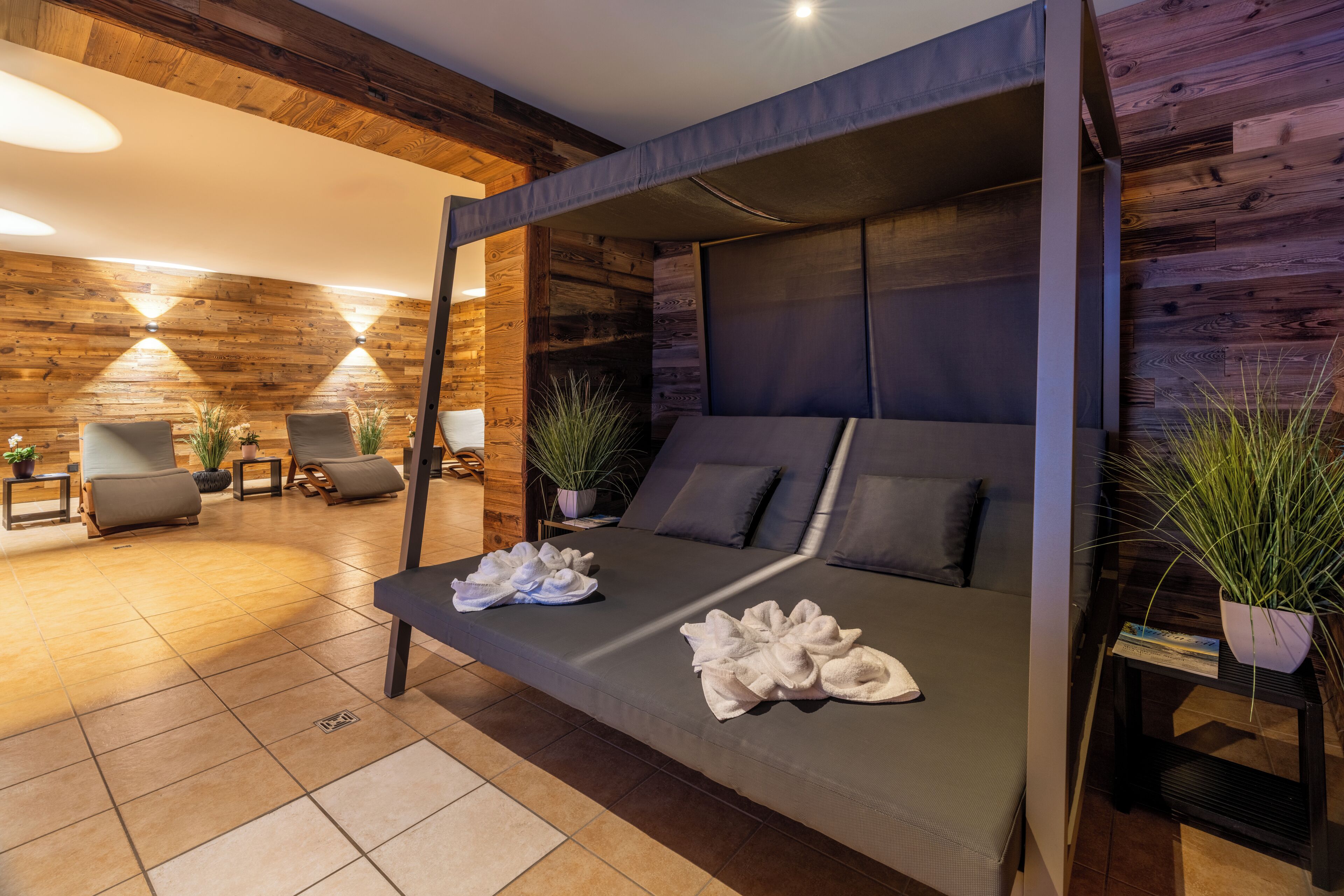 A modern room with a sofa bed, a small table with towels, and a potted plant.