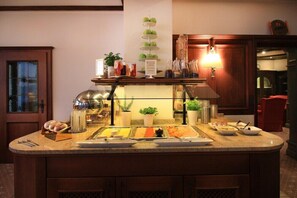 A buffet setup with various food items, a tiered fruit display, and a lamp.