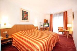 A hotel room with a bed, desk, chair, TV, and a painting on the wall.