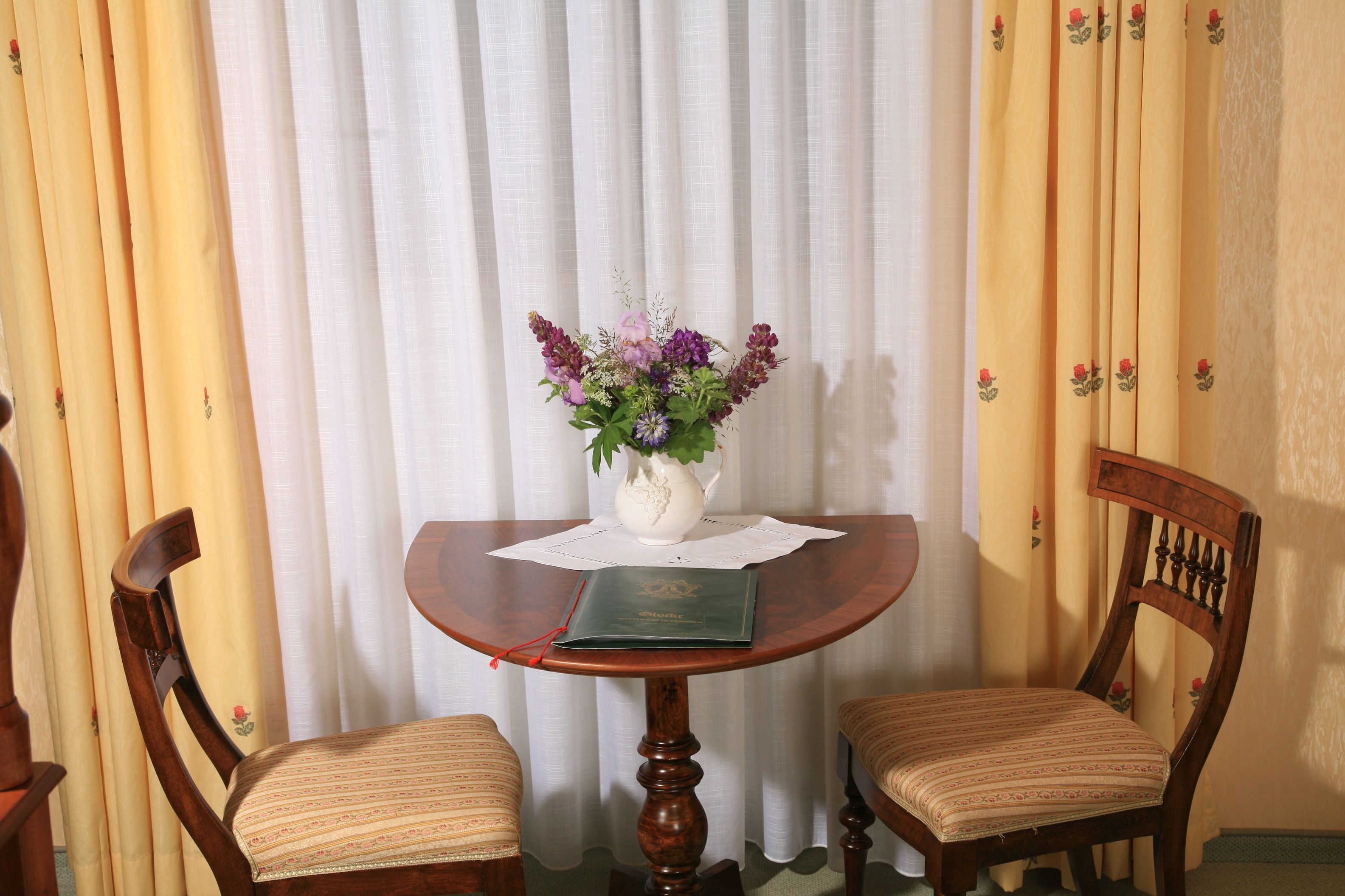 Een houten tafel met een bloemenvaas, twee stoelen en een boek erop.