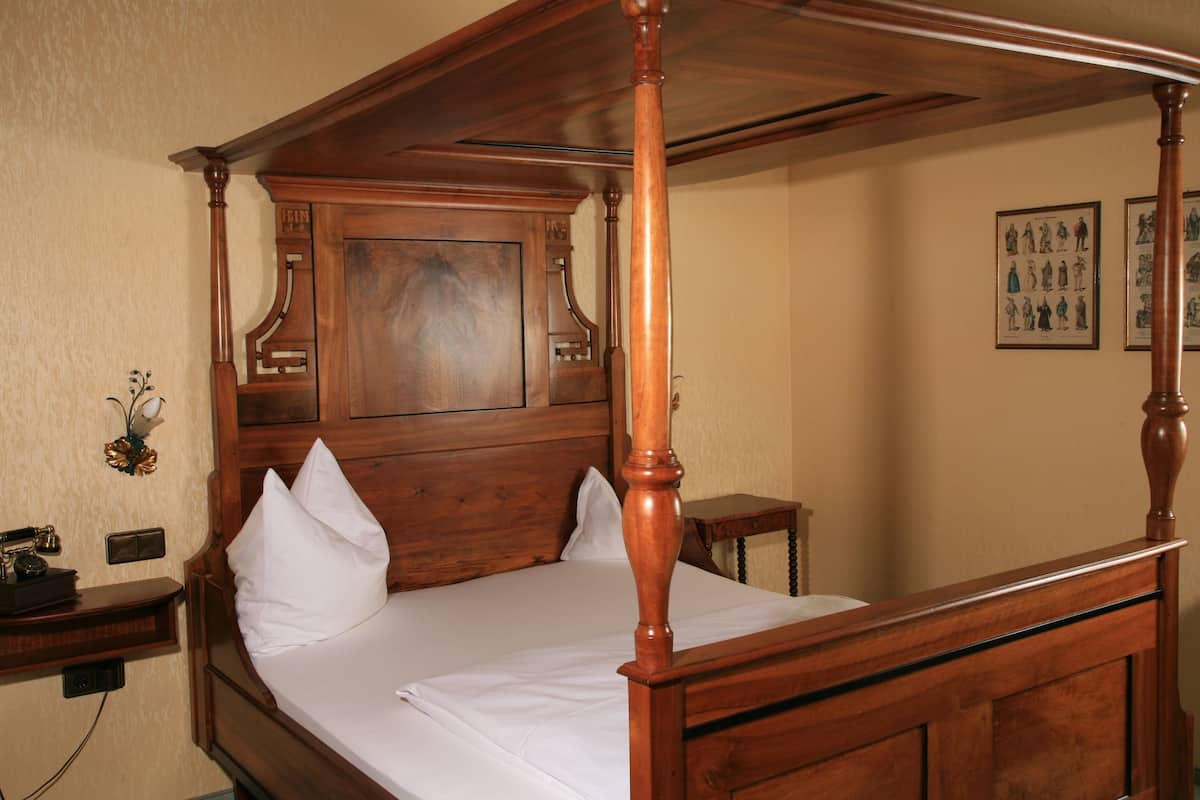Una cama con dosel, cabecera y piecera de madera, una mesita de noche y un teléfono instalado en la pared.