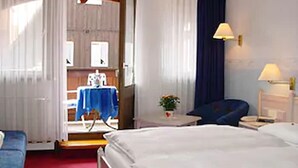 Habitación de hotel con una cama, una silla, una mesita con lámpara y vistas a una zona de cocina.