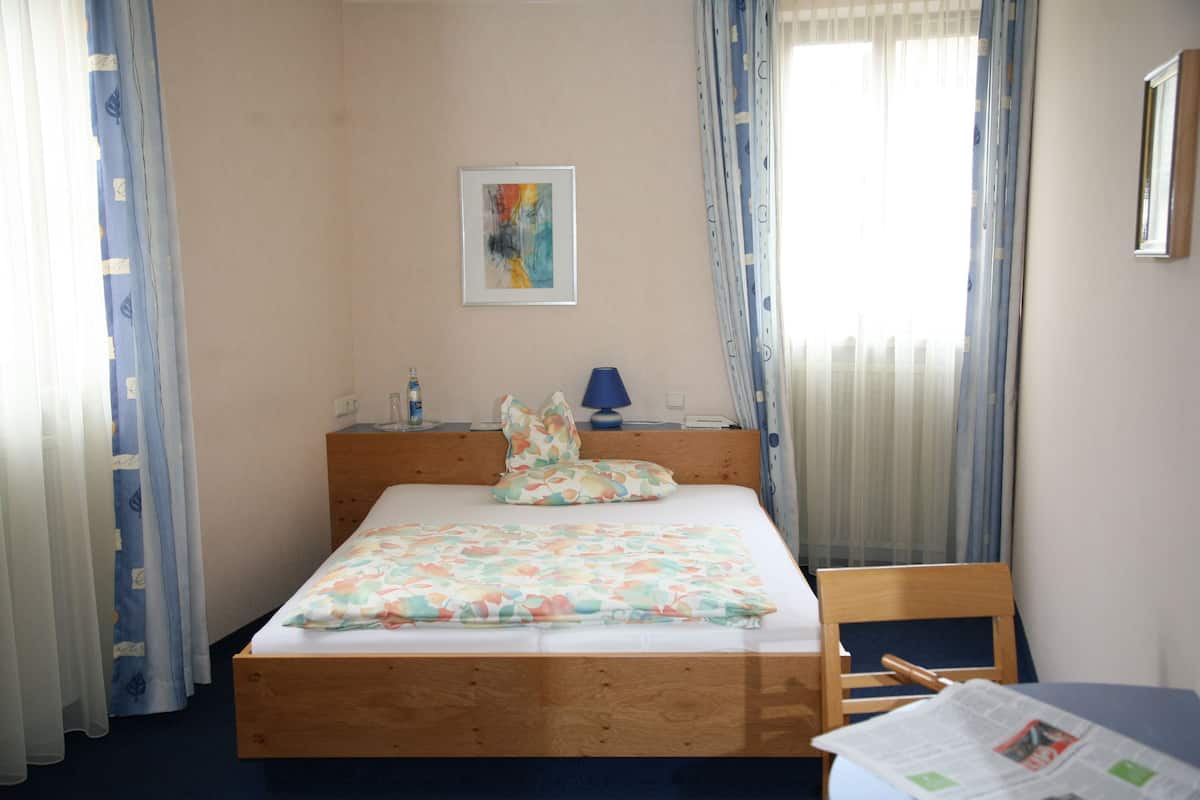 Un dormitorio con una cama de madera, una mesita de noche con lámpara, una silla y un cuadro en la pared.