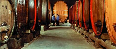 Una bodega con hileras de barriles de madera, suelo de hormigón y una persona a lo lejos.