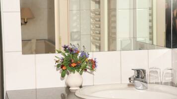 Une salle de bain avec un lavabo blanc, un miroir et un vase de fleurs.