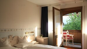Una habitación de hotel con cama, mesita de noche, lámpara y ventana con vistas a zonas verdes.