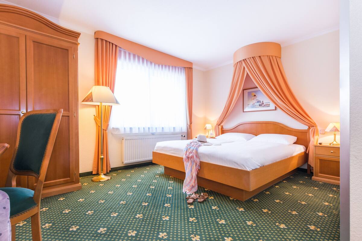 Ein Hotelzimmer mit einem großen Bett, einem Sessel, einem Nachttisch, einer Lampe und einem Fenster mit Vorhängen.