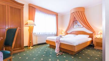 A hotel room with a large bed, a chair, a nightstand, a lamp, and a window with curtains.