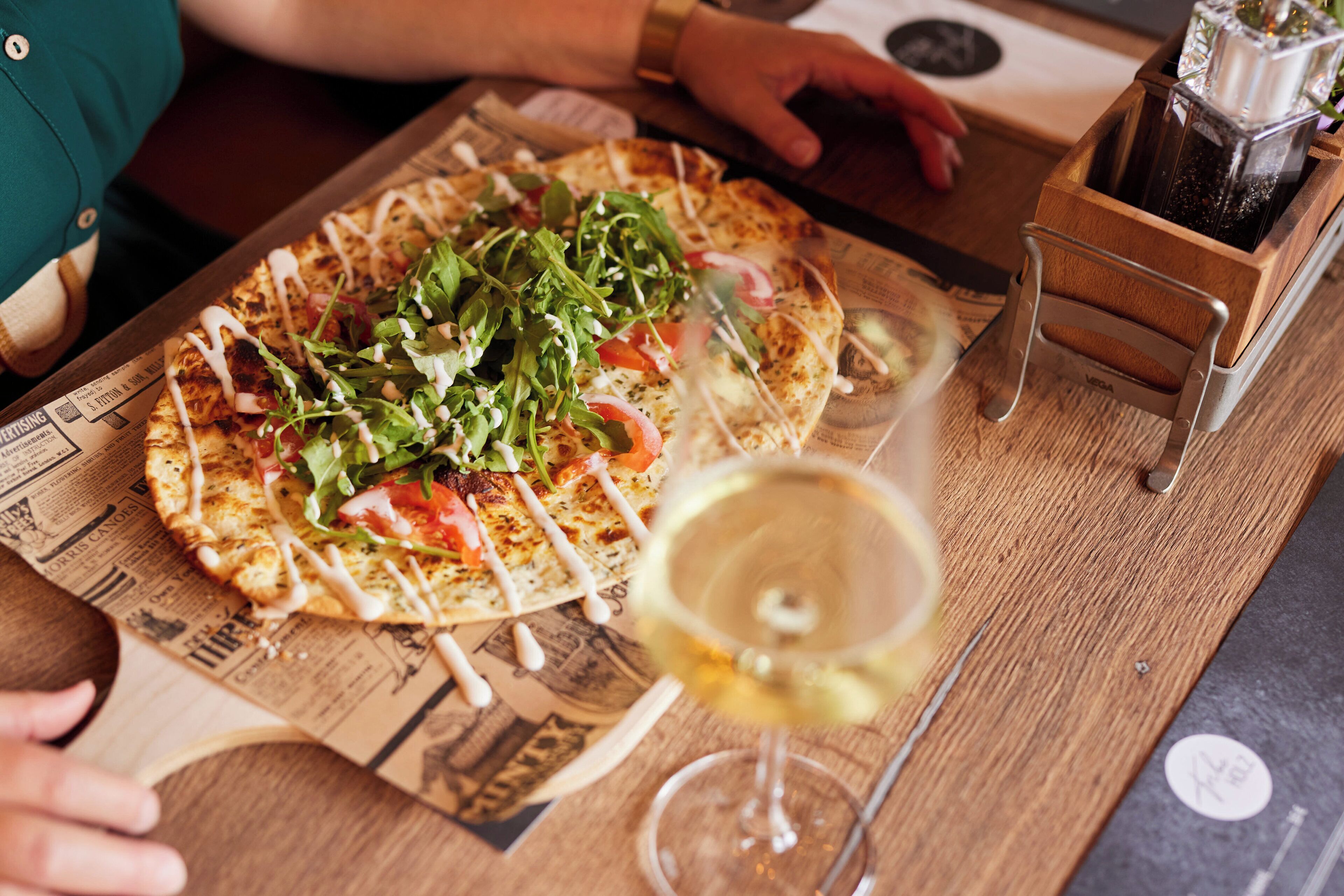 A pizza on a wooden cutting board with a glass of white wine.