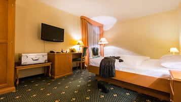 A hotel room with a bed, a desk with a suitcase, a television, and two lamps.