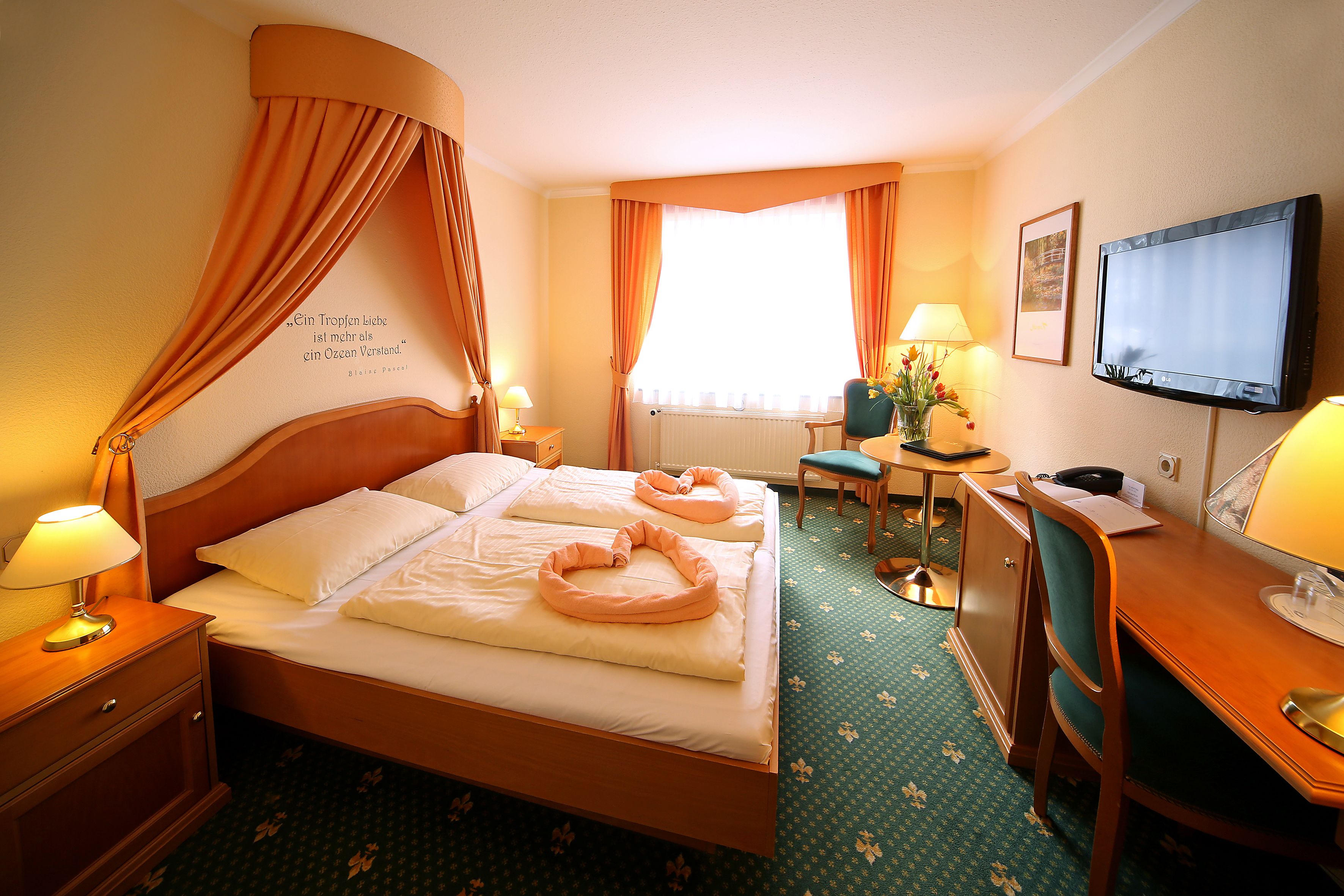 Une chambre d’hôtel équipée d’un lit, d’un bureau, d’une chaise, d’une télévision et d’une fenêtre avec des rideaux.