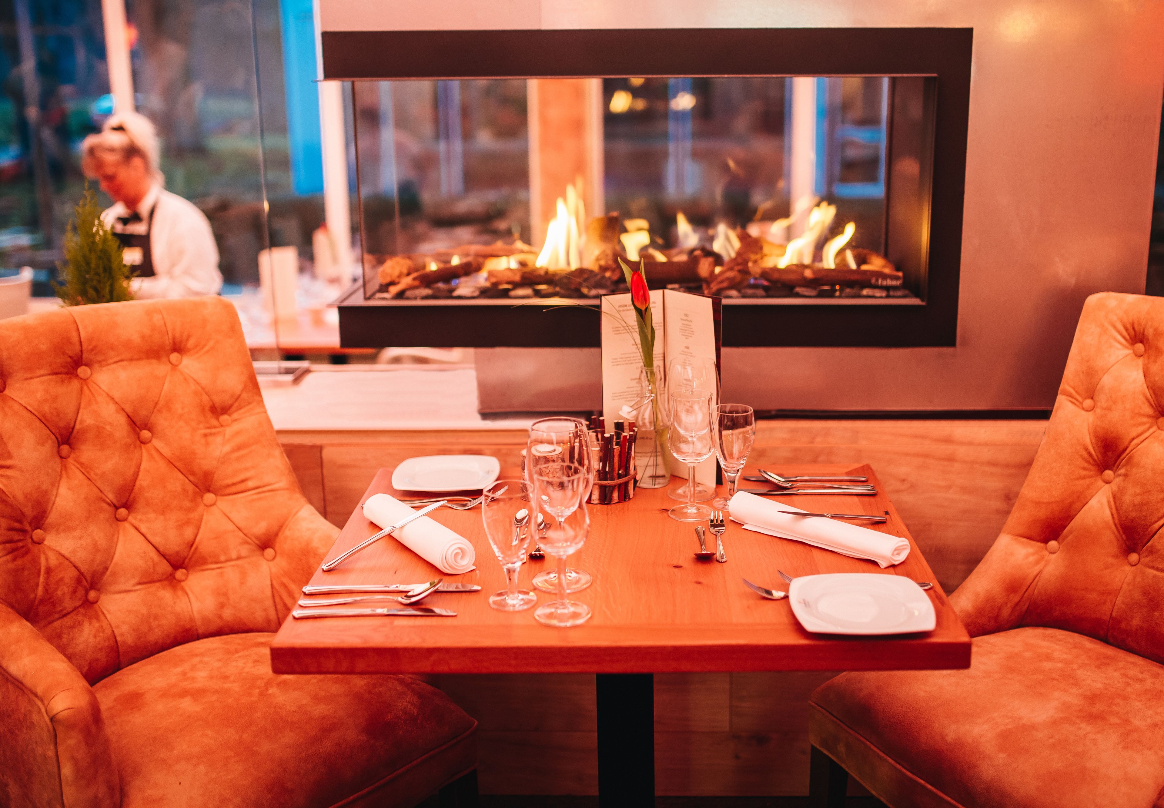 A dining table set for two with a fireplace in the background.
