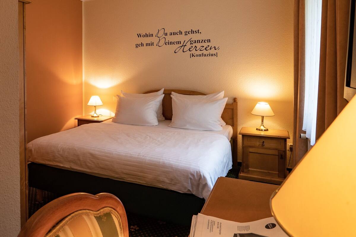 Ein Hotelzimmer mit einem Bett, zwei Nachttischlampen, einer Wand mit einem Zitat und einem Holznachttisch.