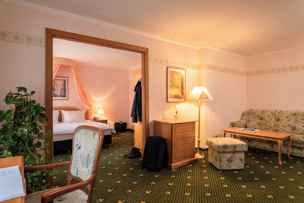 Ein Hotelzimmer mit einem Bett, einem Sessel, einem Sofa, einem Schreibtisch, einer Lampe, einem Schminktisch und einer Pflanze.