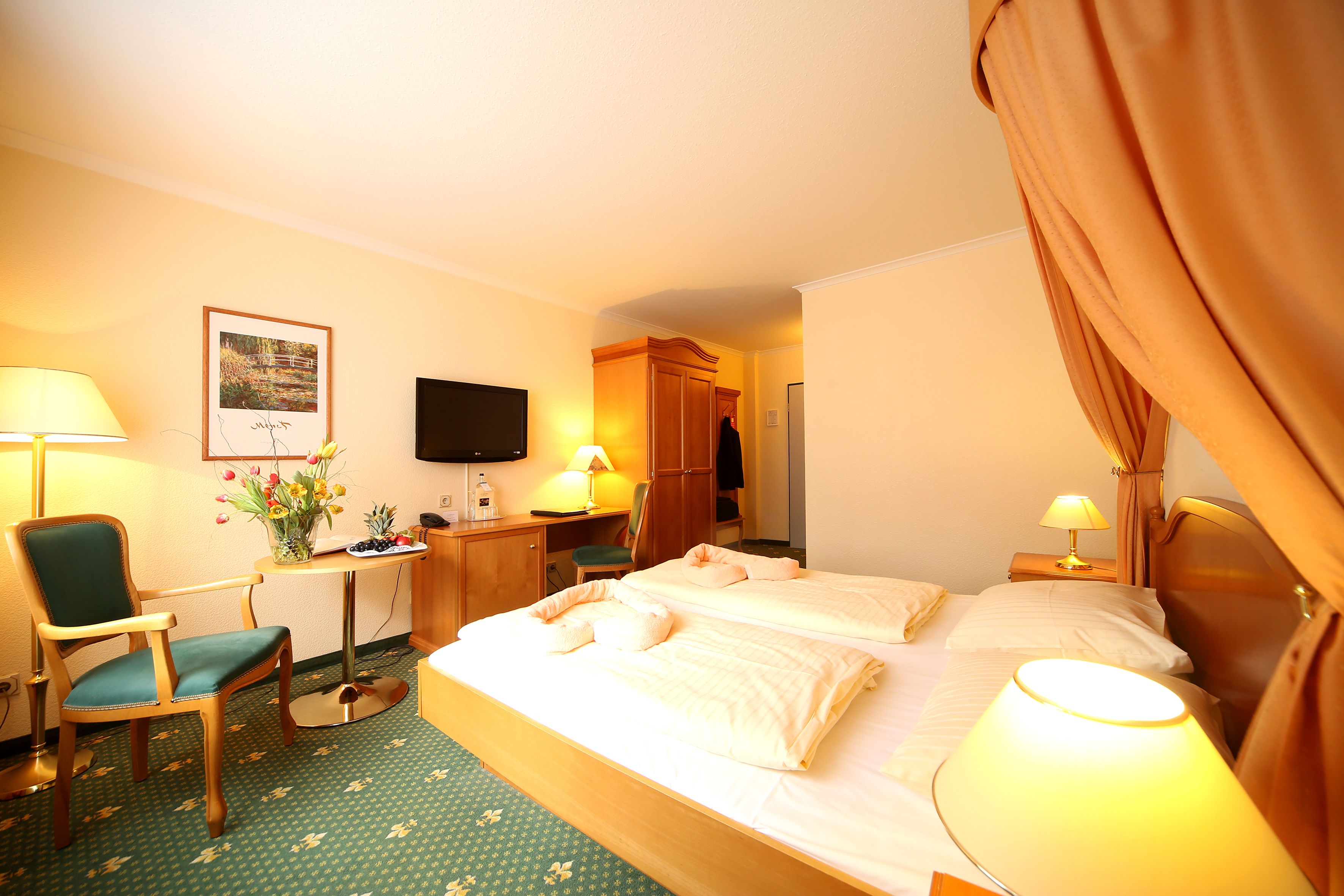 A hotel room with a bed, two bedside lamps, a desk with a chair, a TV, and a wardrobe.