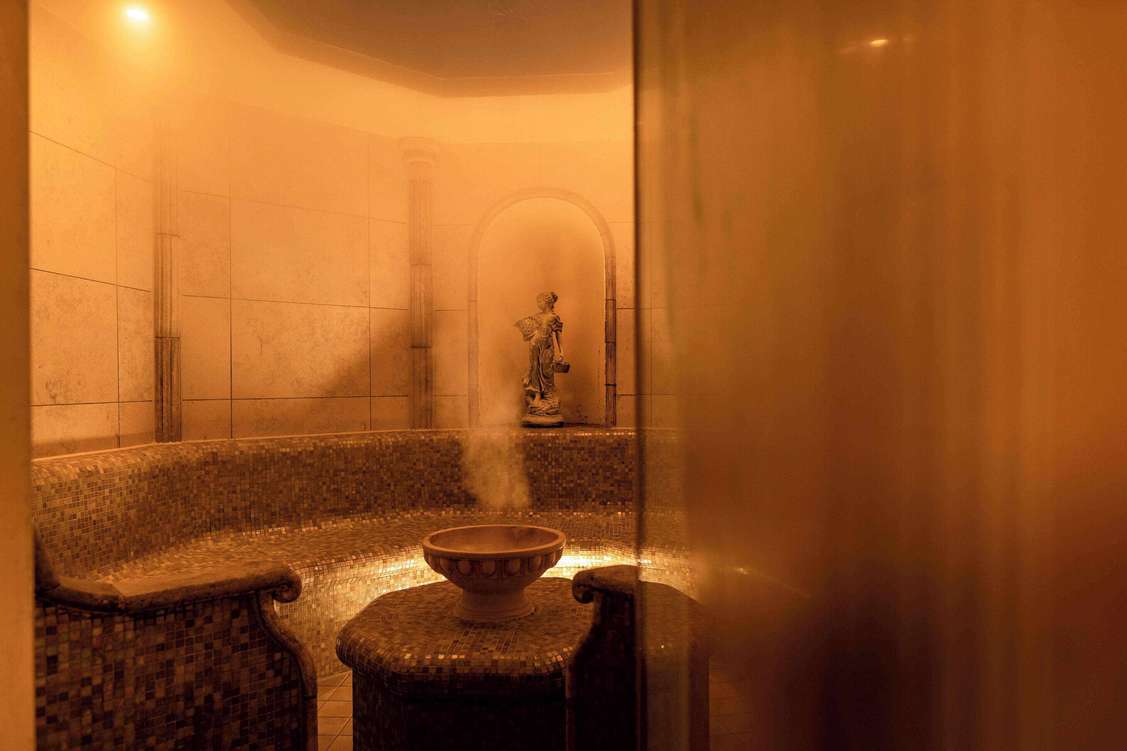 Un baño de vapor con un banco de mosaicos y una estatua al fondo.