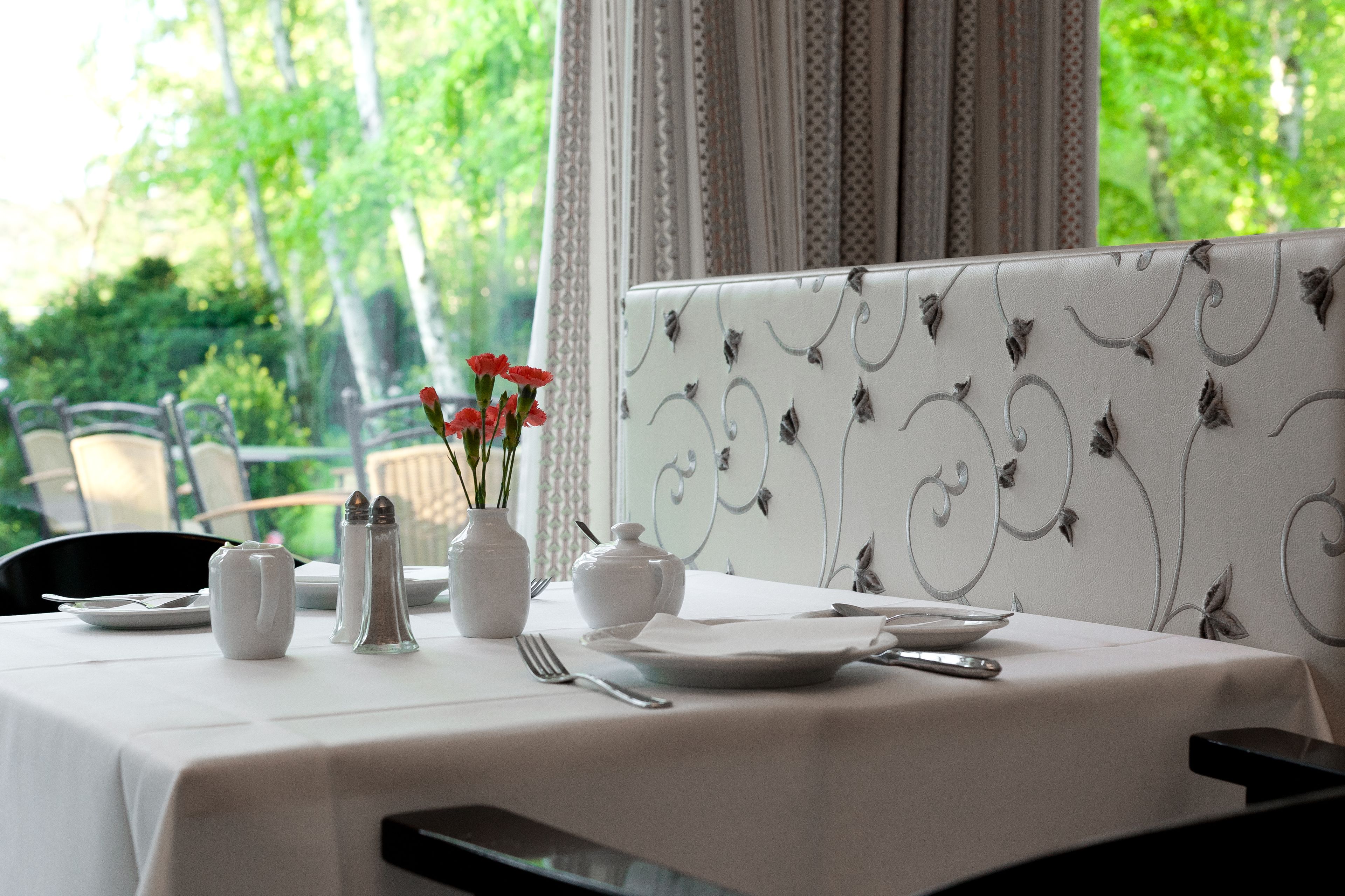 A dining table set with white tablecloth, plates, cutlery, and a vase with flowers.