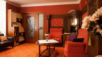 Una habitación con alfombra roja, un armario de madera, un sofá rojo, una pequeña mesa con un jarrón y una estantería.