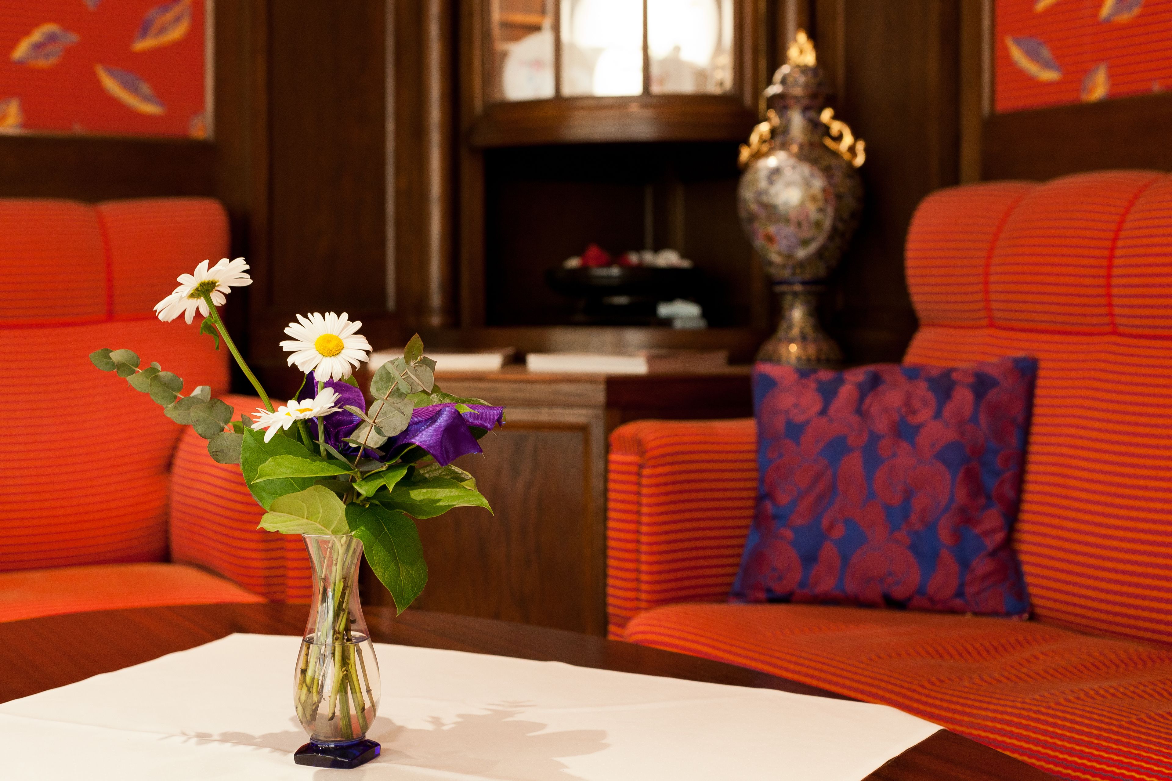 Una habitación con un jarrón de flores sobre una mesa, un sofá con un cojín estampado y una lámpara decorativa.