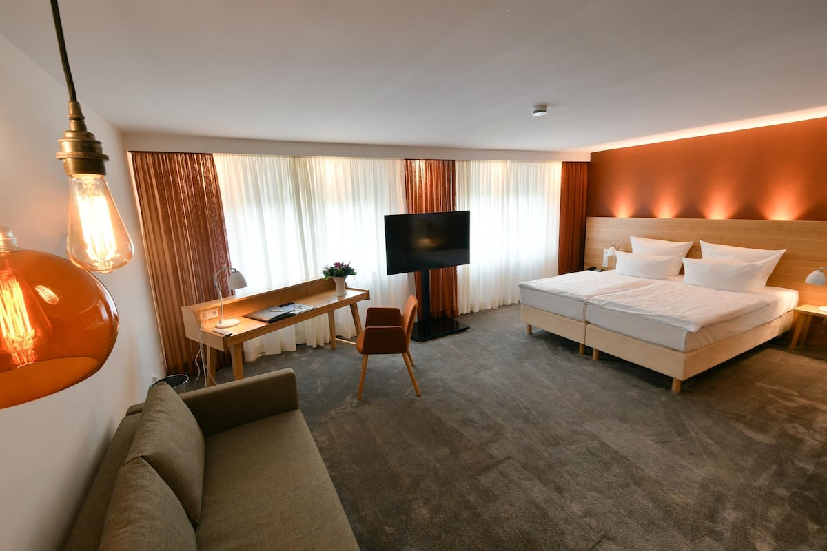 Quarto de hotel com uma cama, uma escrivaninha, uma cadeira, uma televisão e um sofá.
