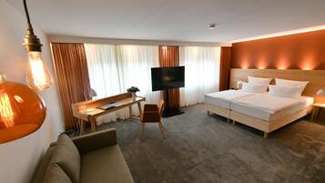 Quarto de hotel com uma cama, uma escrivaninha, uma cadeira, uma televisão e um sofá.