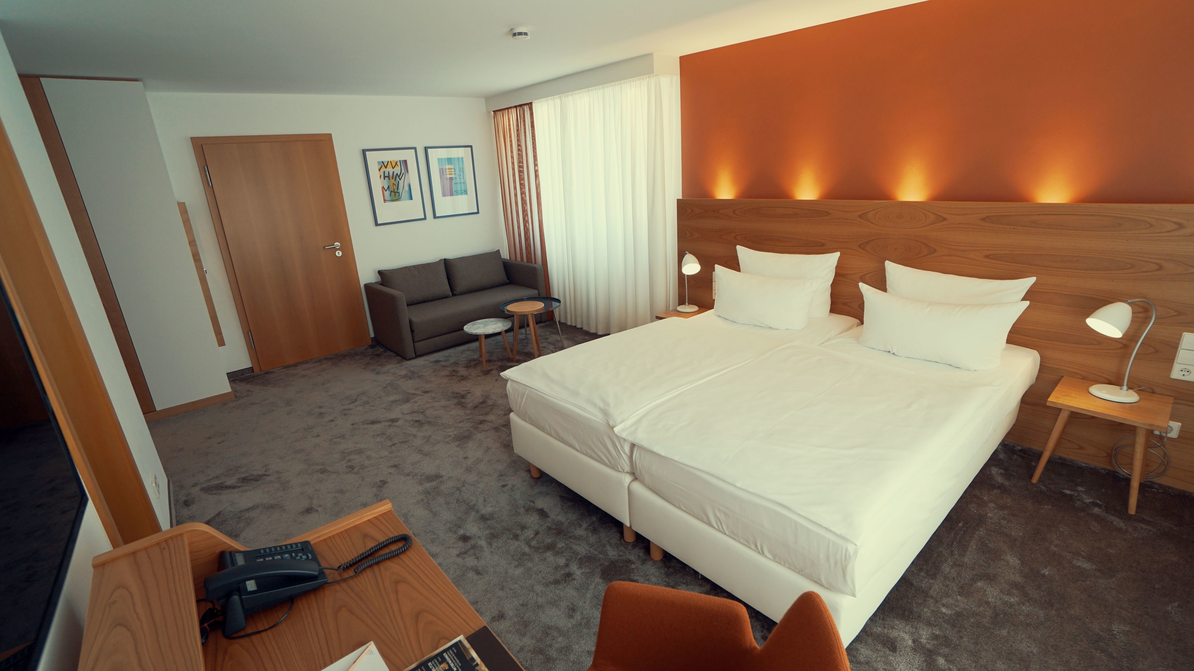 A hotel room with a large bed, a sofa, a desk with a phone, and a bedside table with a lamp.
