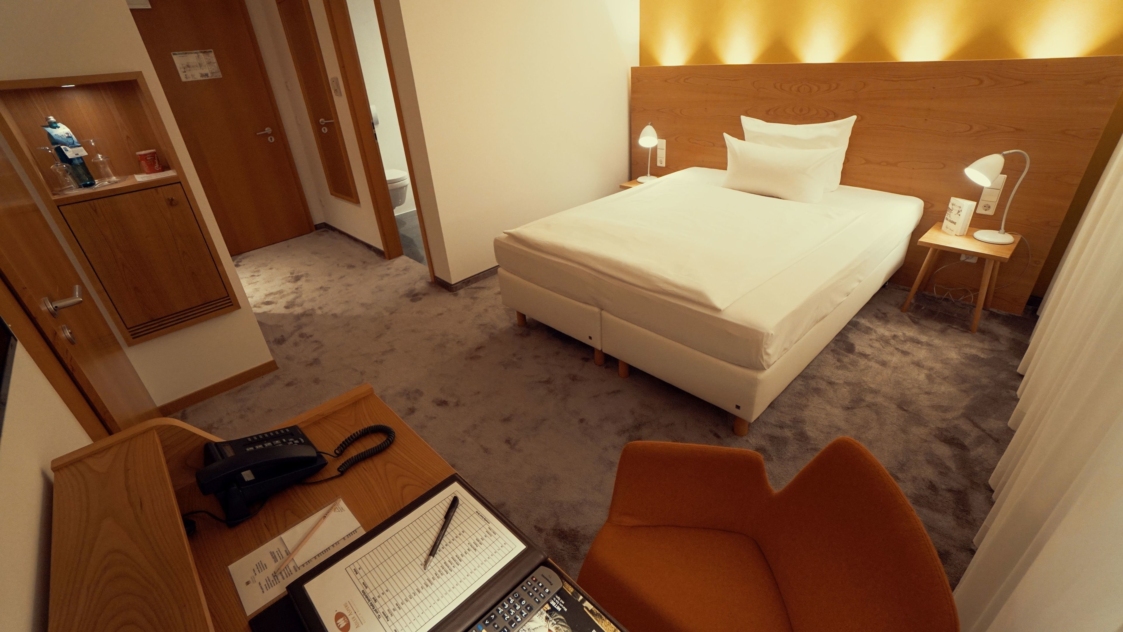 Ein Hotelzimmer mit Bett, Nachttischlampen, einem Schreibtisch mit Telefon und einem Sessel.