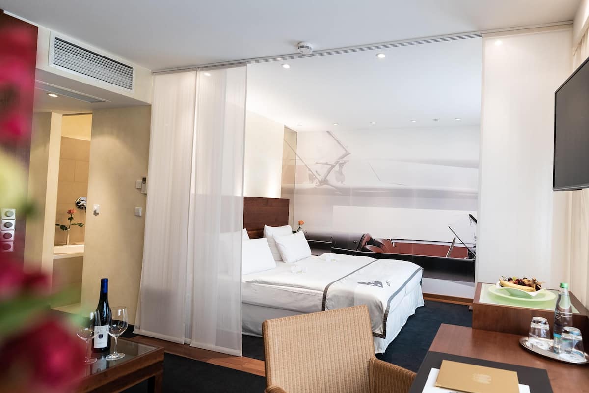 Quarto de hotel com cama, cadeira, escrivaninha, televisão e janela com vista para um barco.