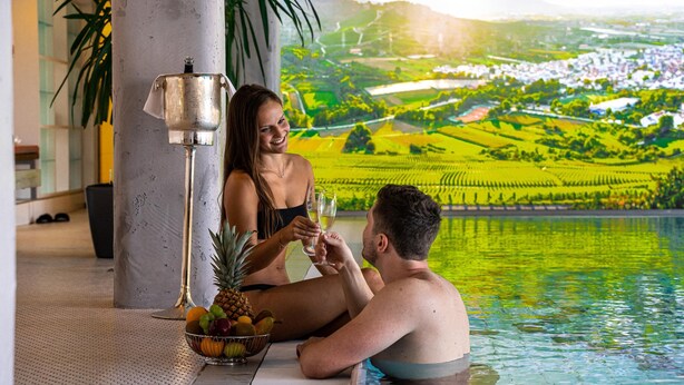 Un couple se détend au bord d’une piscine, avec une vue sur des champs en terrasses.