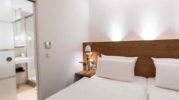 A hotel room with a wooden headboard, a bedside table with a lamp, and a large bed with white bedding.