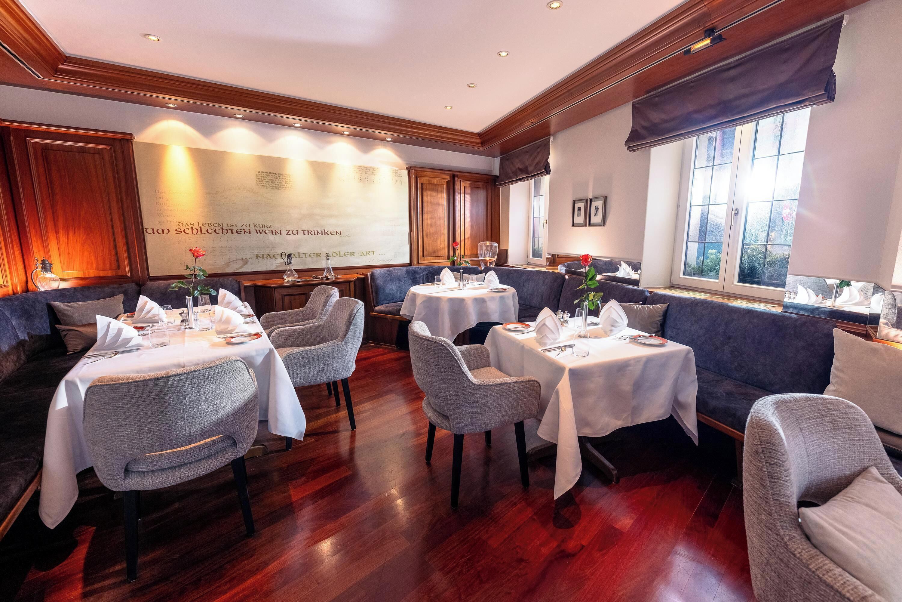 A restaurant with multiple tables and chairs, wooden flooring, and large windows.