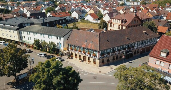 An aerial view of a hotel with a traditional European architectural style, featuring a prominent entrance with a tiled roof and a large window display.