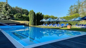 A swimming pool with lounge chairs and umbrellas, surrounded by trees. - Hotel & Spa Sommerfeld - Adults Only (Kremmen)