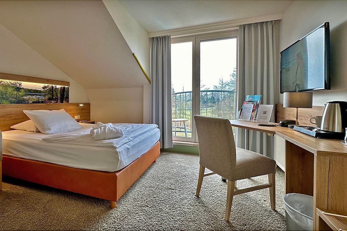 A hotel room with a bed, a desk, a chair, a TV, and a window with curtains.