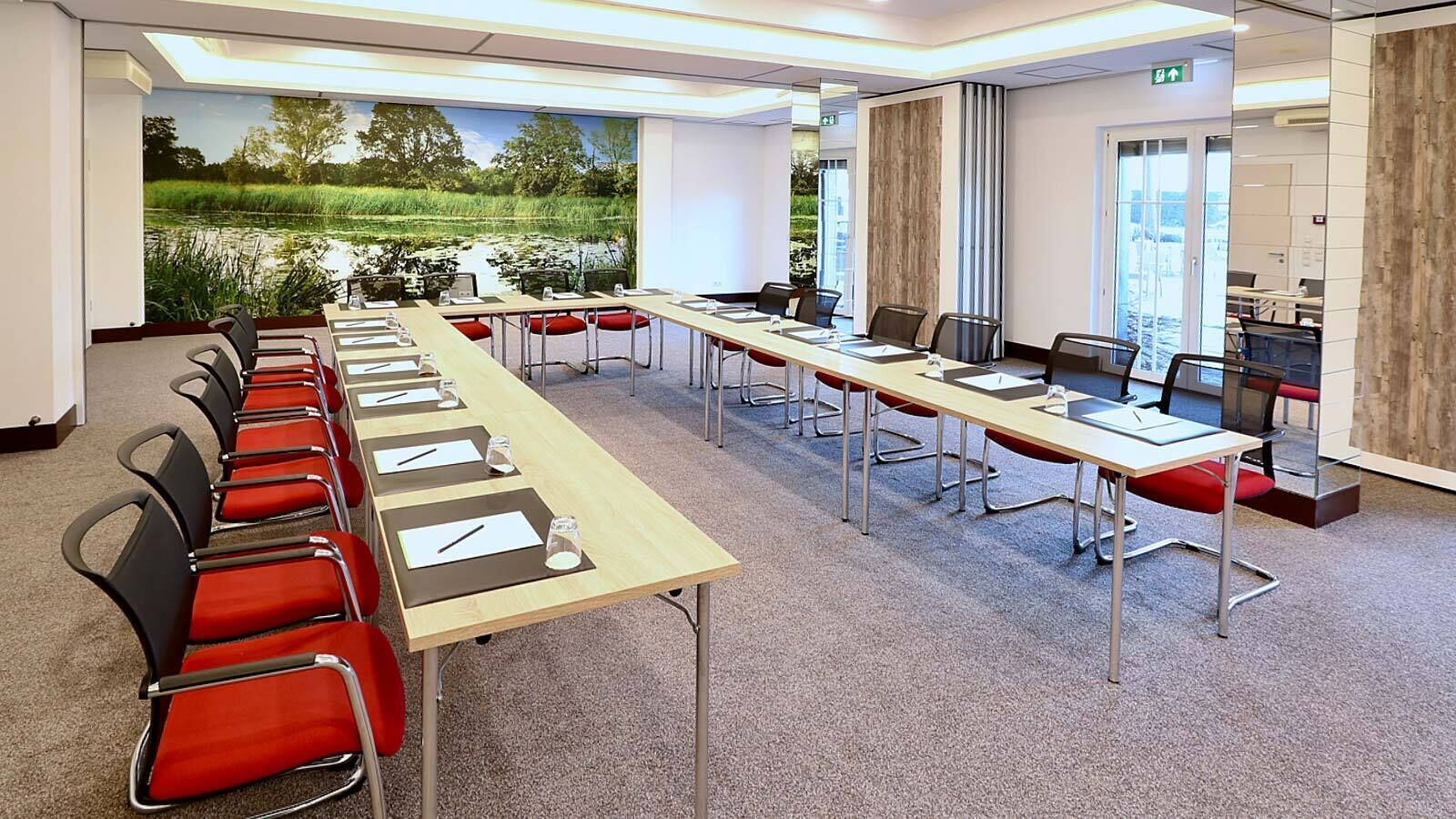 A conference room with long tables, red chairs, and a large window with a view of a pond.