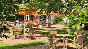 An outdoor cafe with wicker furniture and a yellow awning with the name "Schofferhofer". - Hotel & Spa Sommerfeld - Adults Only (Kremmen)