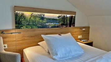 A bedroom with a bed, a nightstand, a chair, and a wall-mounted painting of a forest scene.