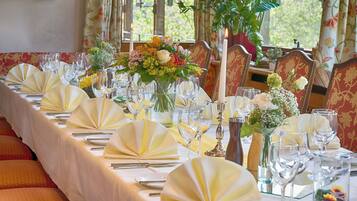 A long dining table set with white tablecloths, yellow napkins, and glassware, surrounded by red upholstered chairs.