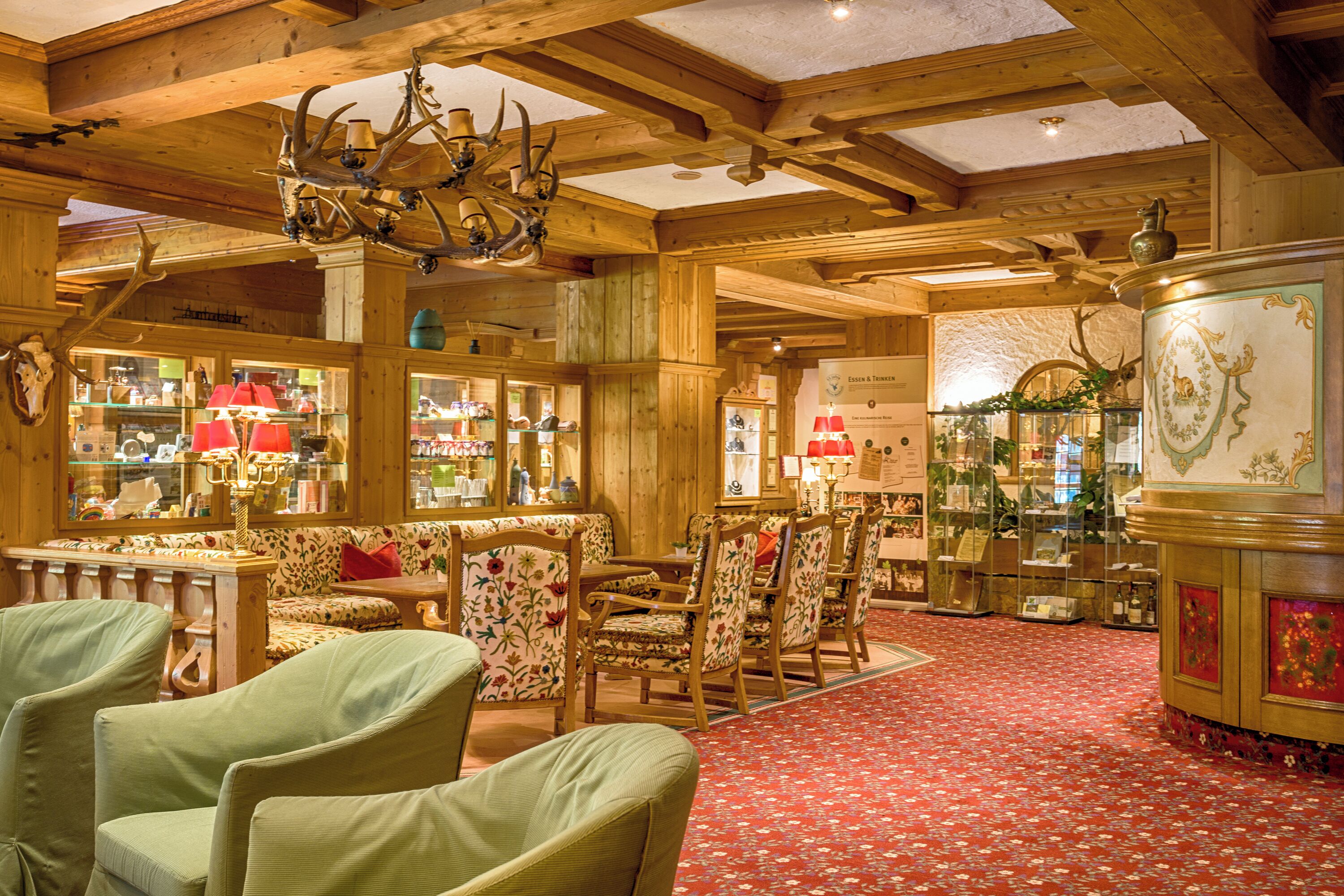 Un intérieur en bois agrémenté d’un tapis à motifs rouges, de meubles en bois et de lustres ornés de bois de cerf.