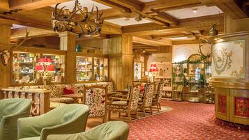 Un intérieur en bois agrémenté d’un tapis à motifs rouges, de meubles en bois et de lustres ornés de bois de cerf.