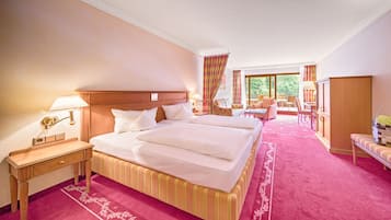 Une chambre d’hôtel avec un grand lit, une table de chevet en bois, un bureau et une chaise. Il y a une fenêtre avec des rideaux et une vue sur l’extérieur.
