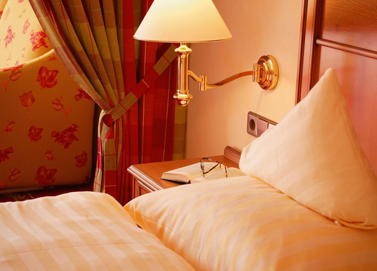 Une chambre d’hôtel avec un lit, une table de chevet avec une lampe, une fenêtre avec des rideaux et un téléphone fixé au mur.