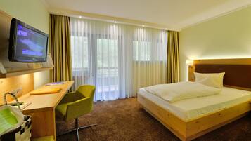 Habitación de hotel con cama, escritorio, silla, televisor y ventana con cortinas.