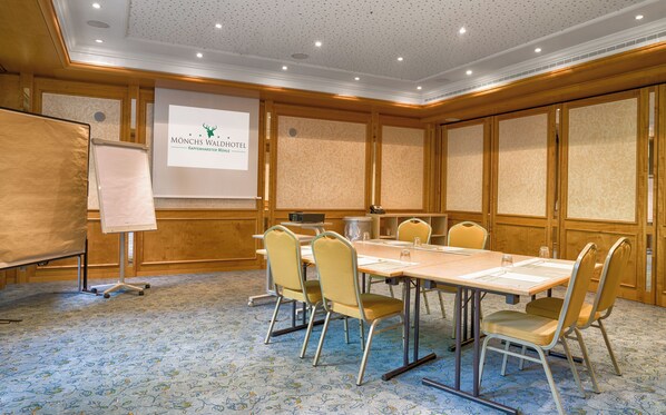 Una sala de conferencias con una mesa grande, seis sillas, una pantalla de proyector y una pizarra.